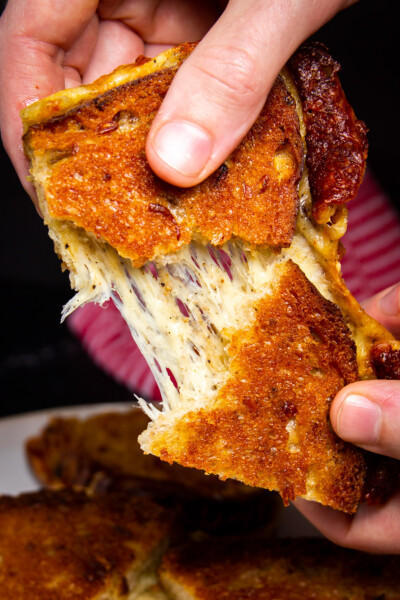 A close up shot of the smoked grilled cheese being pulled apart by two hands.