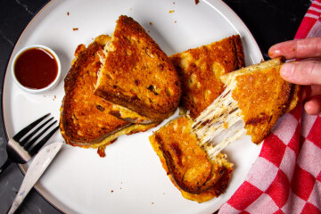 A few slices of a smoked grilled cheese sandwich with a long cheese pull.