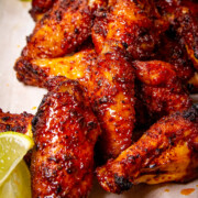 A close up of some smoked Traeger wings piled on a board with lime wedges beside.