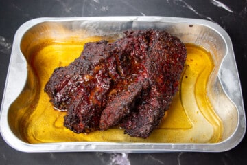 The smoked chuck roast in a tray with beef stock.