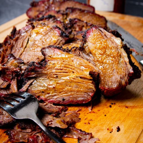 A close up shot of the poor mans brisket on a cutting board with a fork and spice rub in the background.