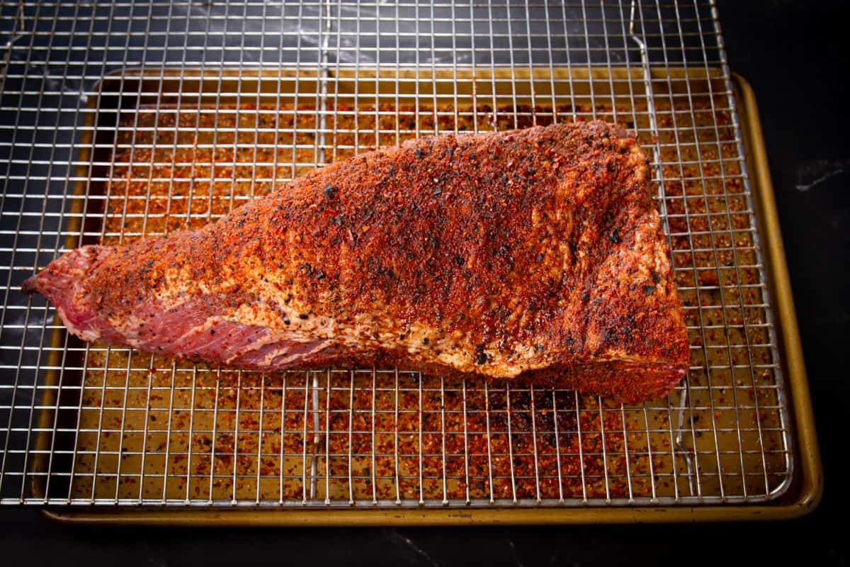 The tri tip marinated overnight on a resting rack with a baking tray underneath.