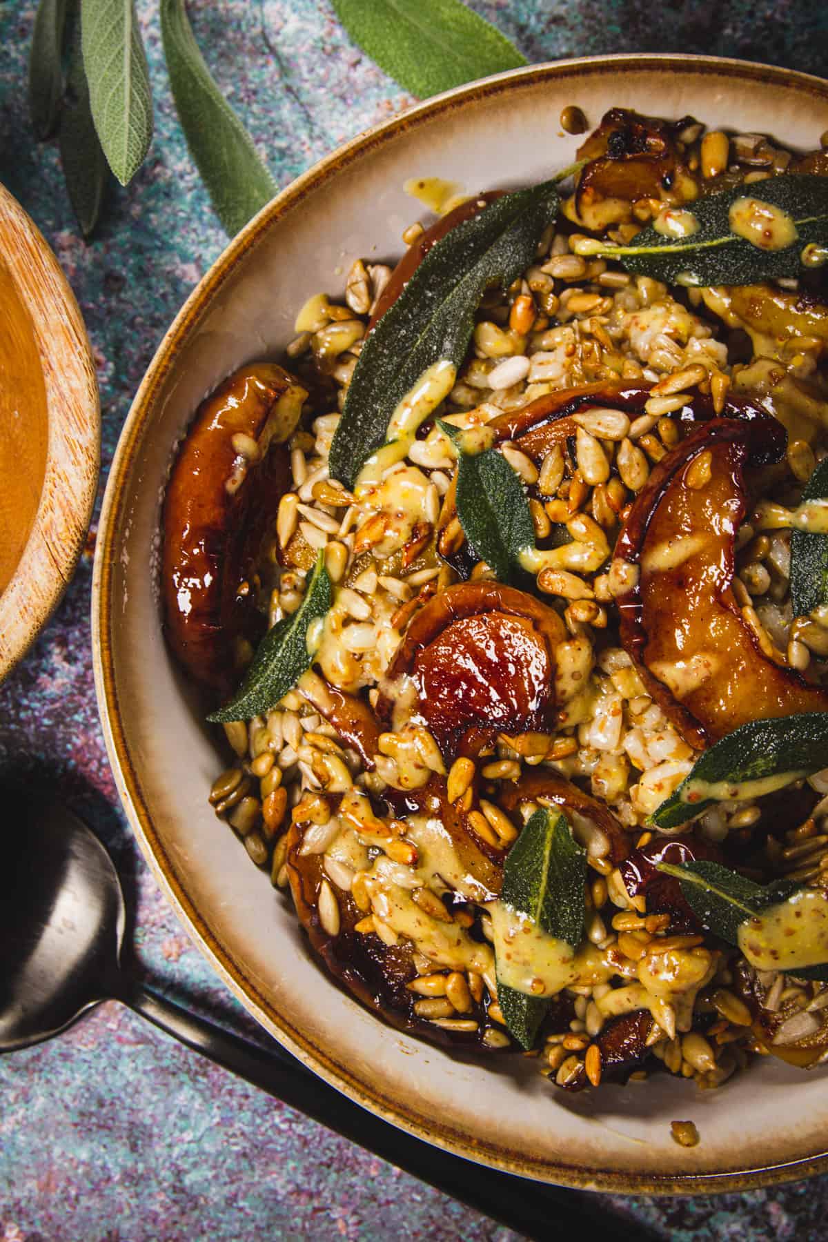 Roasted apple spelt salad in a bowl with sage leaves and a spoon beside it.